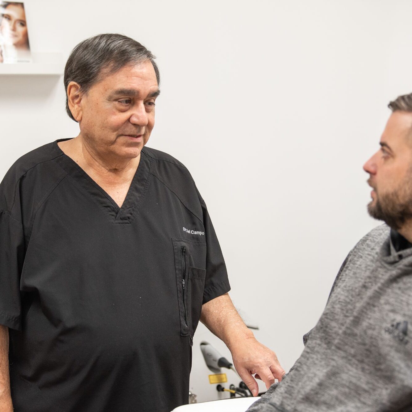 Dr. Danilo Del Campo consulting with a patient in a dermatology office, wearing a black medical coat, emphasizing personalized care at Chicago Skin Clinic.
